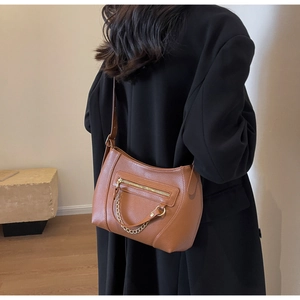 Detail view of brown pebbled leather crossbody bag with gold chain on black coat