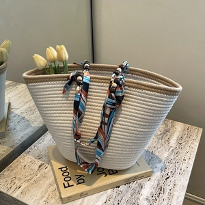 Fashionable woven tote bag with silk scarf handle and wooden beads on marble surface