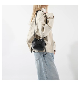 Detail showing crocodile texture on small black bucket bag worn by model