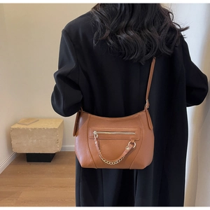 Detail view of caramel brown pebbled leather crossbody bag with gold chain on black coat