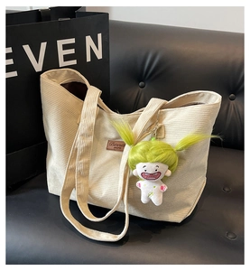 Detail of cream corduroy tote bag with plush doll pendant on a black leather sofa