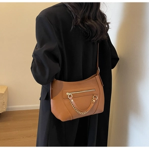 Detail showing tan leather crossbody bag with pebble texture and gold chain on black blazer