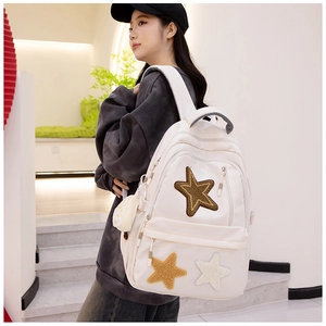 Detail of white canvas backpack featuring three plush star patches and side pendant accessory