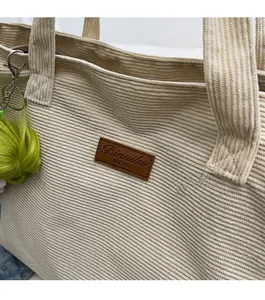 Detail of corduroy tote bag featuring a brown faux leather label and green fluffy pompom