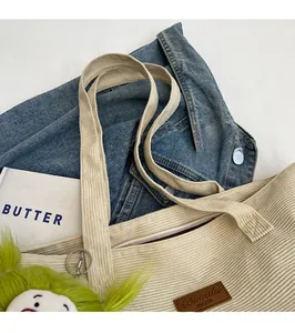 Close-up of beige corduroy tote bag with zipper closure and green plush keychain charm