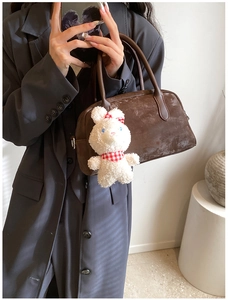 Dettaglio borsa in pelle scamosciata marrone scuro con ciondolo a forma di coniglio bianco