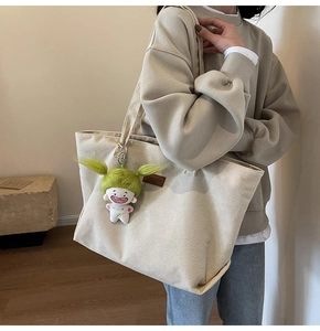 Detail shot of cream corduroy tote bag with plush doll charm and leather brand logo