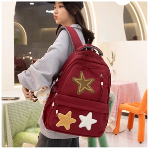 Detail of dark red canvas backpack with plush star patches worn by model in a cafe