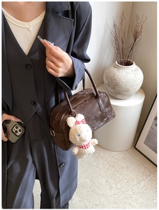 Dettaglio di borsa in pelle PU marrone scuro con ciondolo a coniglio tenuta da modella