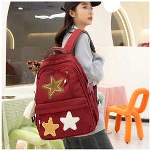 Detail of burgundy canvas backpack with three decorative stars worn by a model