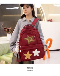Detail of dark red canvas backpack showing star patches and plush egg-shaped pendant charm