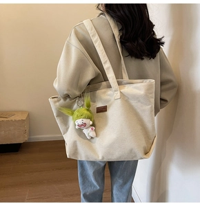 Back view of a large off-white corduroy tote bag with wide straps and cartoon pendant
