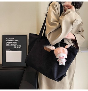 Detail of black corduroy tote bag with brown logo patch and cute doll pendant on model