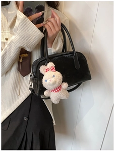 Dettaglio di una borsa Boston nera con ciondolo a forma di coniglio bianco e tracolla fine