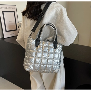 Silver quilted tote bag with black wide strap worn as crossbody over grey sweatshirt