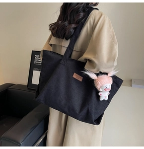 Detail of black corduroy tote bag with leather logo and cute pink doll charm on shoulder
