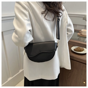 Close-up of black PU saddle bag with patterned strap shown on a model in a cafe