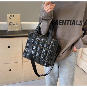 Detail of black quilted puffy tote bag showing shiny nylon texture and crossbody strap