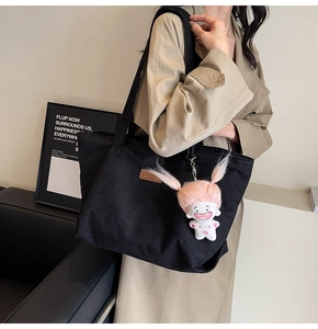 Detail of black corduroy tote bag featuring a brown leather tag and pink doll charm
