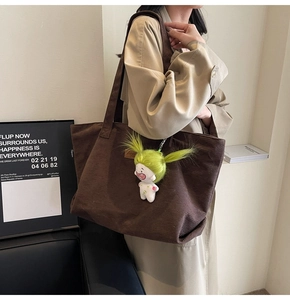 Detail of coffee corduroy tote bag with quirky green doll pendant and brand leather tag