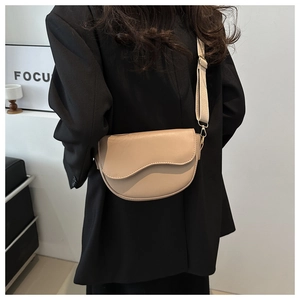 Close-up of minimalist beige saddle bag featuring a unique wavy flap and wide strap