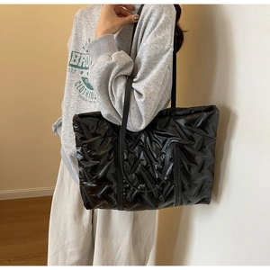 Vue lifestyle d'un grand sac cabas matelassé noir brillant porté à l'épaule par un mannequin