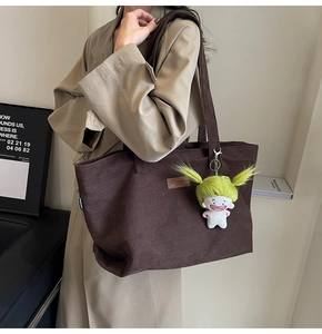 Brown corduroy tote bag detail with leather logo label and cute doll charm accessory