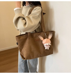Brown corduroy tote bag detail with leather label and pink plush doll charm