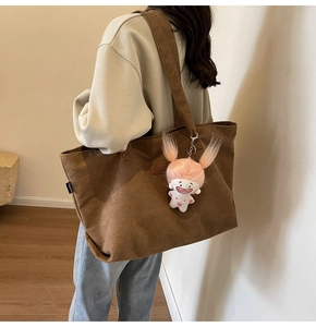 Detailed close-up of brown corduroy tote bag texture with a cute cartoon doll pendant