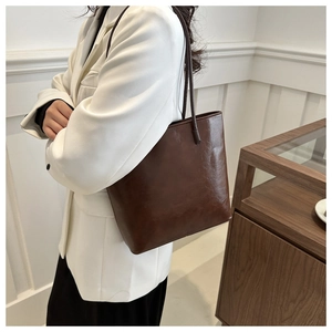 Detail view of deep brown faux leather tote bag worn over the shoulder by a model