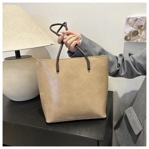 Close-up of the beige PU leather tote bag with dark brown handles in a lifestyle setting