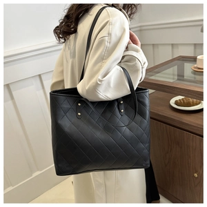 Detail view of a large black quilted tote bag worn in a cozy lifestyle setting