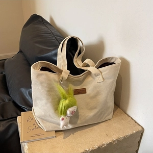 Minimalist beige corduroy tote bag with plush charm on a stone table in a living room