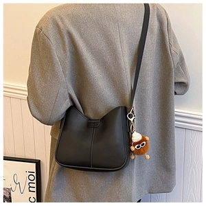 Detail of black leather shoulder bag with a cute brown plush monster charm on the side