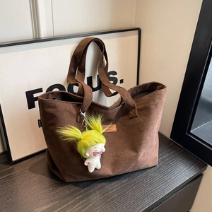 Brown corduroy tote bag for women with a cute character pendant on a dark wooden surface