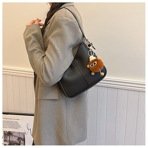 Detail of black matte PU leather shoulder bag with creative brown plush monster charm