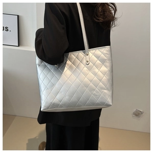 Silver quilted tote bag with diamond lattice pattern worn over the shoulder by a model