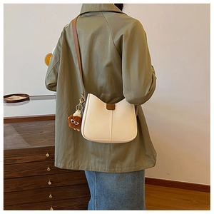Detail view of cream white PU crossbody bag with brown strap and plush lion charm