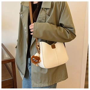 Detail of cream leather shoulder bag with brown strap and plush monster charm