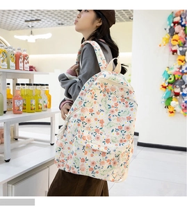 Détail du sac à dos en toile fleurie avec motifs orange et rose et pompon latéral