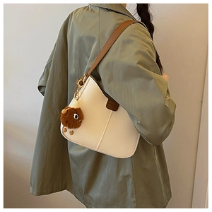 Detail of off-white PU leather shoulder bag with brown strap and fuzzy monster charm