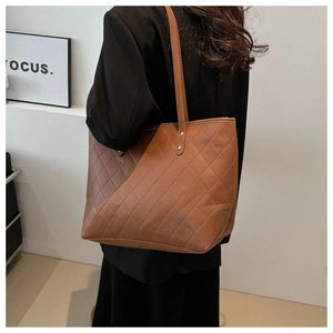 Detailed view of caramel brown quilted PU leather tote bag worn by model over a coat