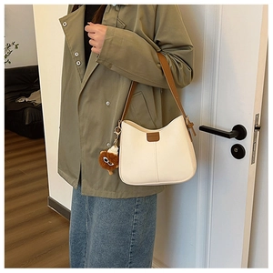 Detail of a beige PU leather shoulder bag featuring a plush charm and brown straps