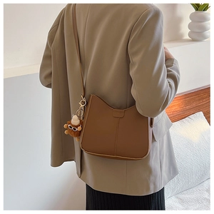 Detail of caramel brown PU leather bag with cute plush monster charm on model shoulder