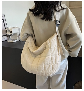 Rear view of a model wearing a cream-white quilted crossbody bag with adjustable wide strap
