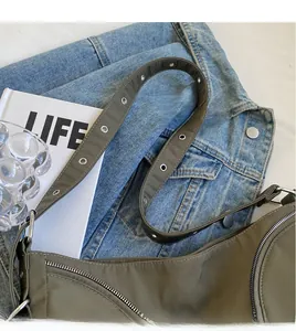 Detail of olive green nylon crossbody bag showing long strap with silver eyelet accents