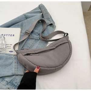 Fashionable grey half-moon crossbody bag in nylon fabric on denim jacket background