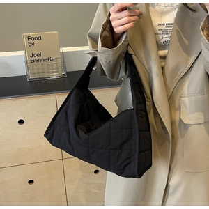 Close-up of black quilted hobo bag with diamond stitching on a beige trench coat