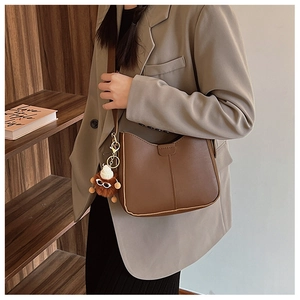 Detail of brown PU leather shoulder bag featuring a cute plush charm and vertical stitching