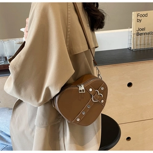 Caramel heart-shaped shoulder bag with silver studs and buckles worn by model